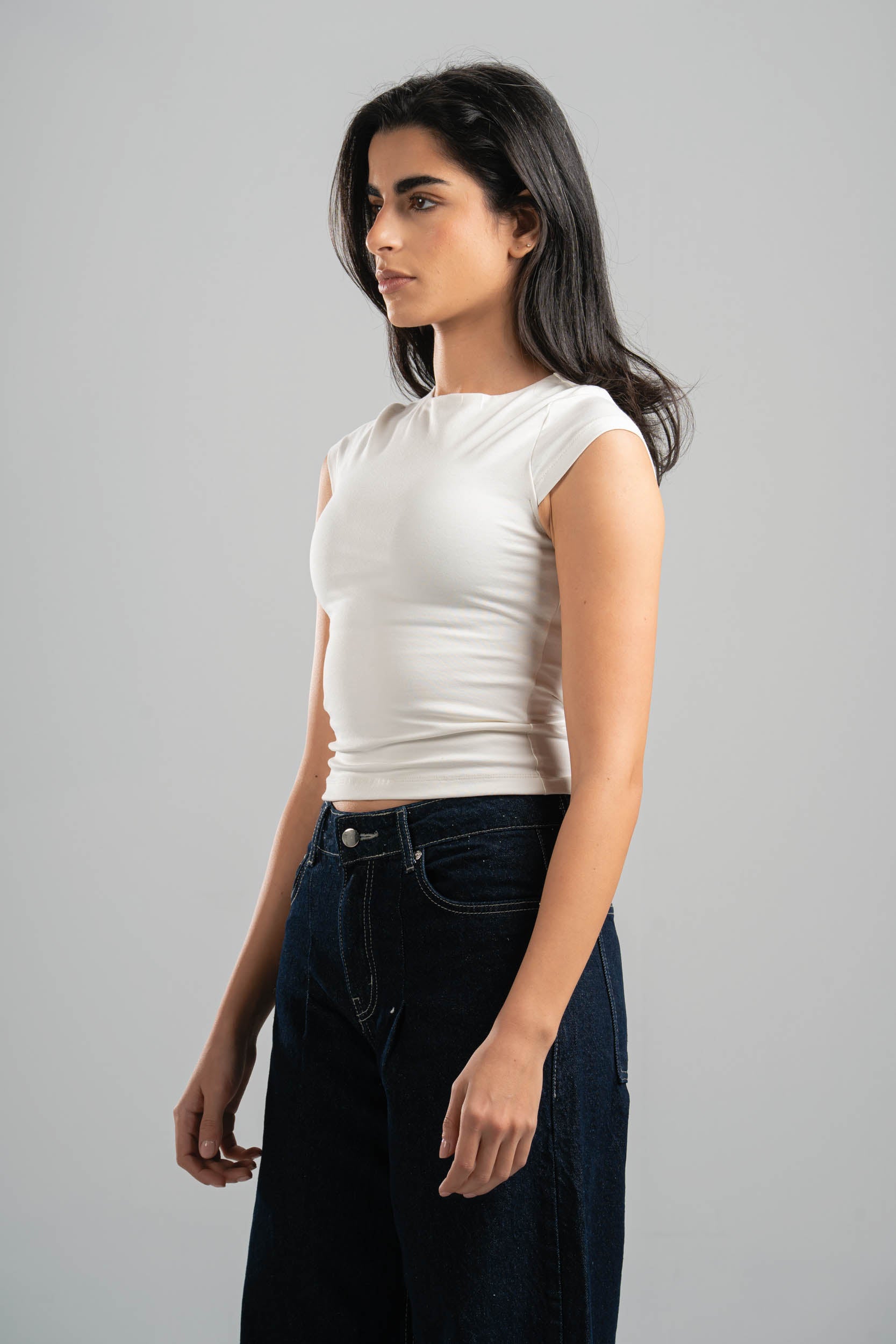 Woman wearing a white sleeveless top and dark jeans on a gray background
