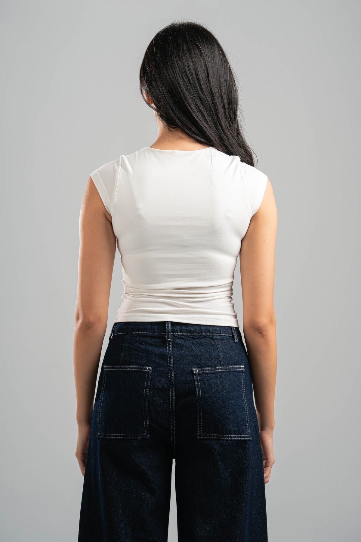 Person wearing a white top and dark jeans against a gray background