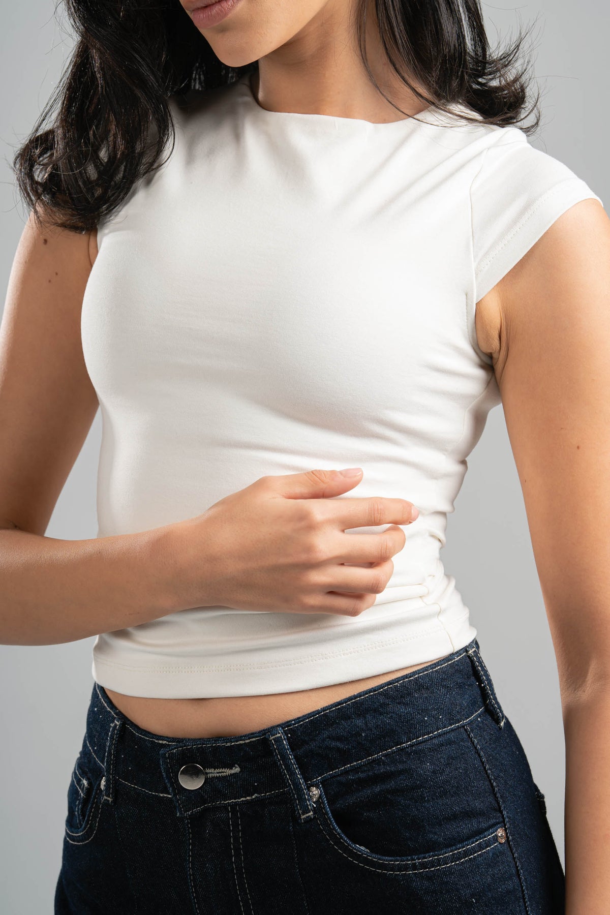 Person wearing a white crop top and dark jeans against a gray background