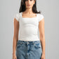 Woman wearing a white top and blue jeans against a gray background