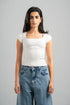 Woman wearing a white top and blue jeans against a gray background