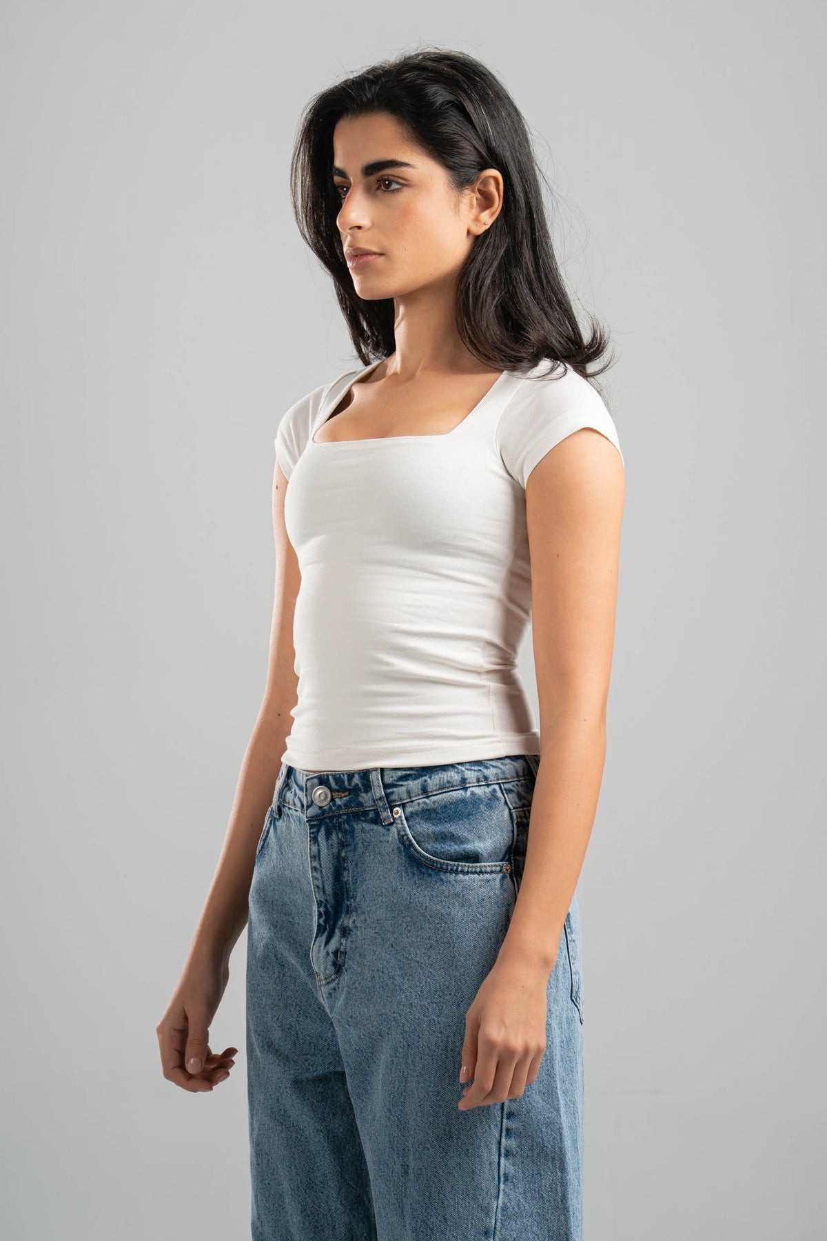 Woman wearing a white t-shirt and blue jeans against a gray background