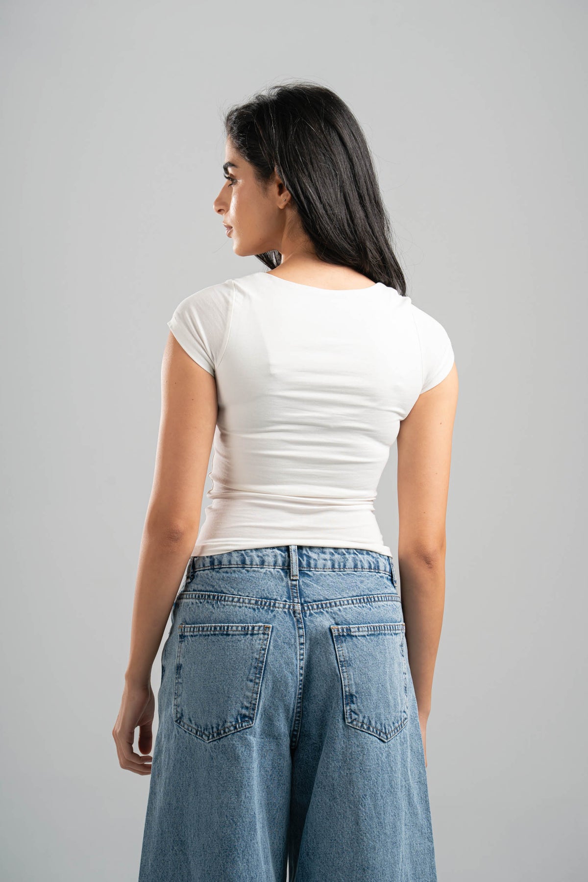Woman wearing a white t-shirt and blue jeans against a gray background