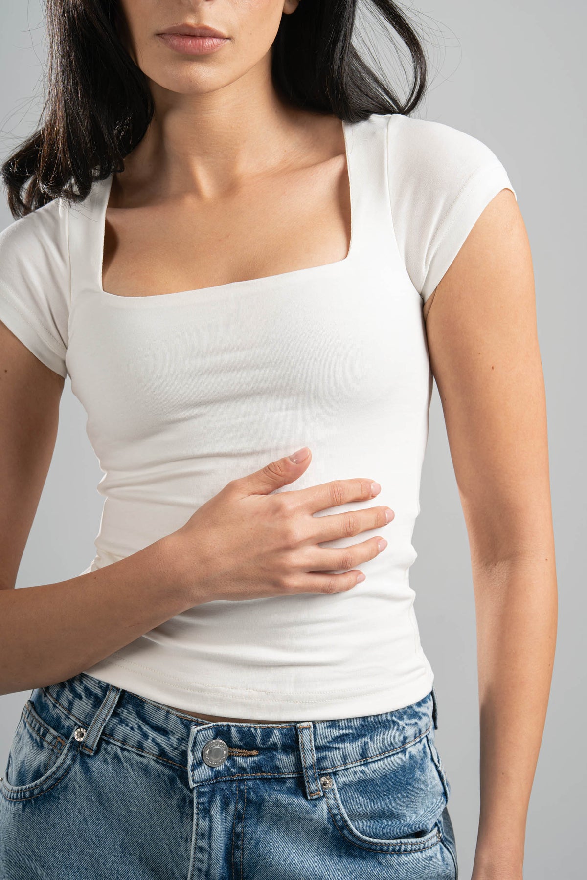Woman wearing a white t-shirt and blue jeans against a gray background