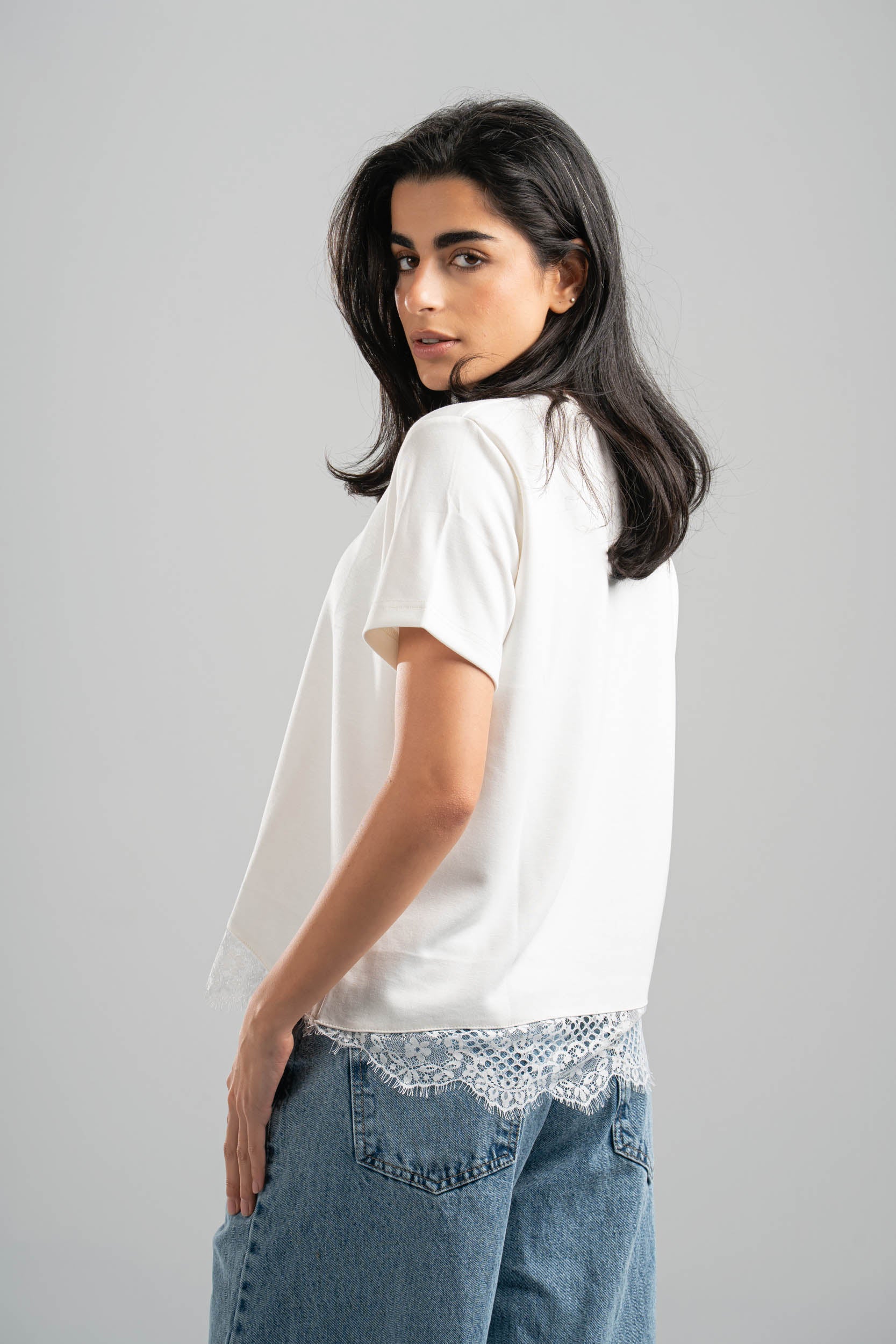 Woman wearing a white t-shirt with lace trim and blue jeans on a gray background