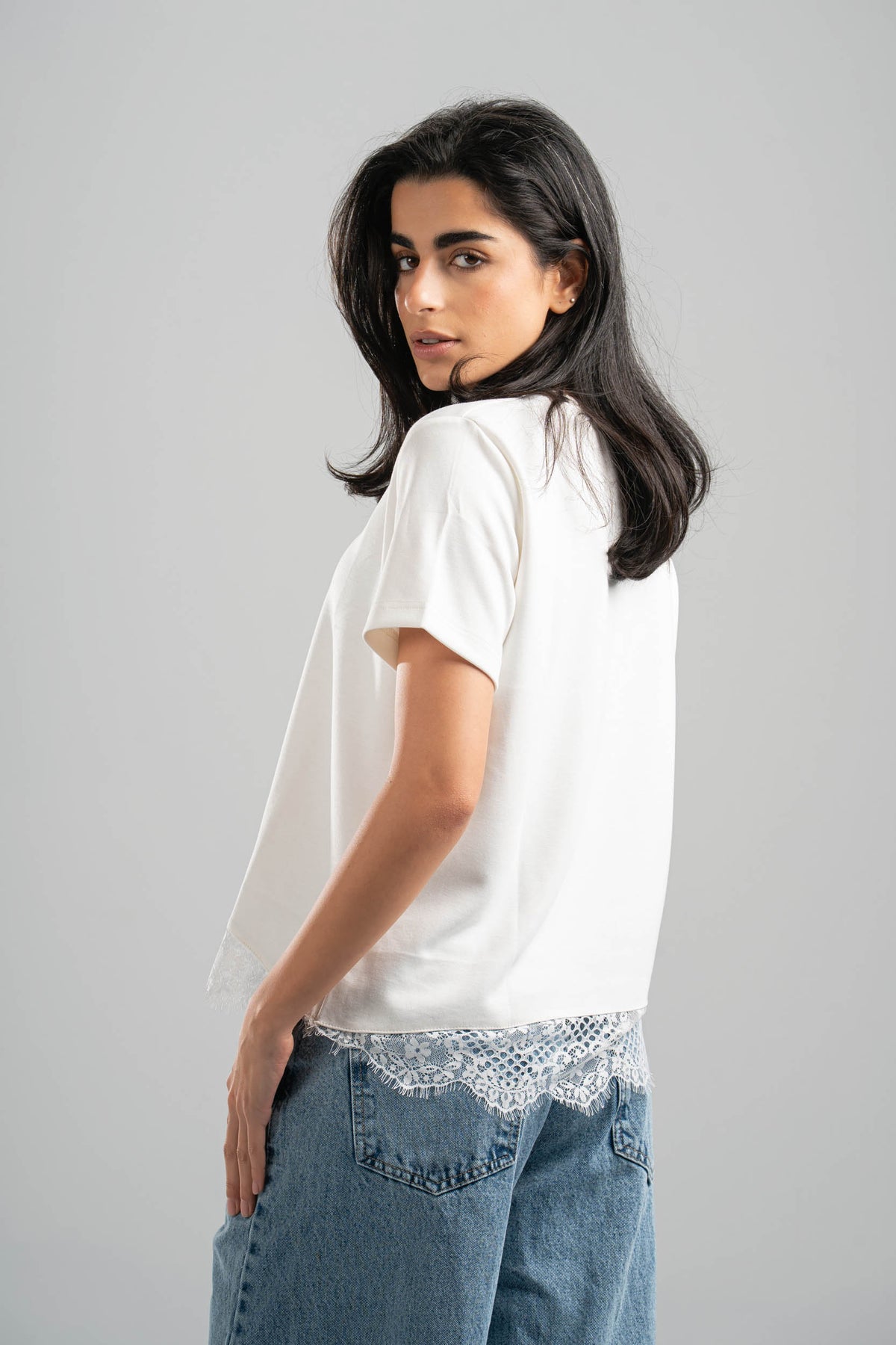 Woman wearing a white t-shirt with lace trim and blue jeans on a gray background