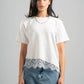 Woman wearing a white t-shirt with lace trim and blue jeans on a gray background