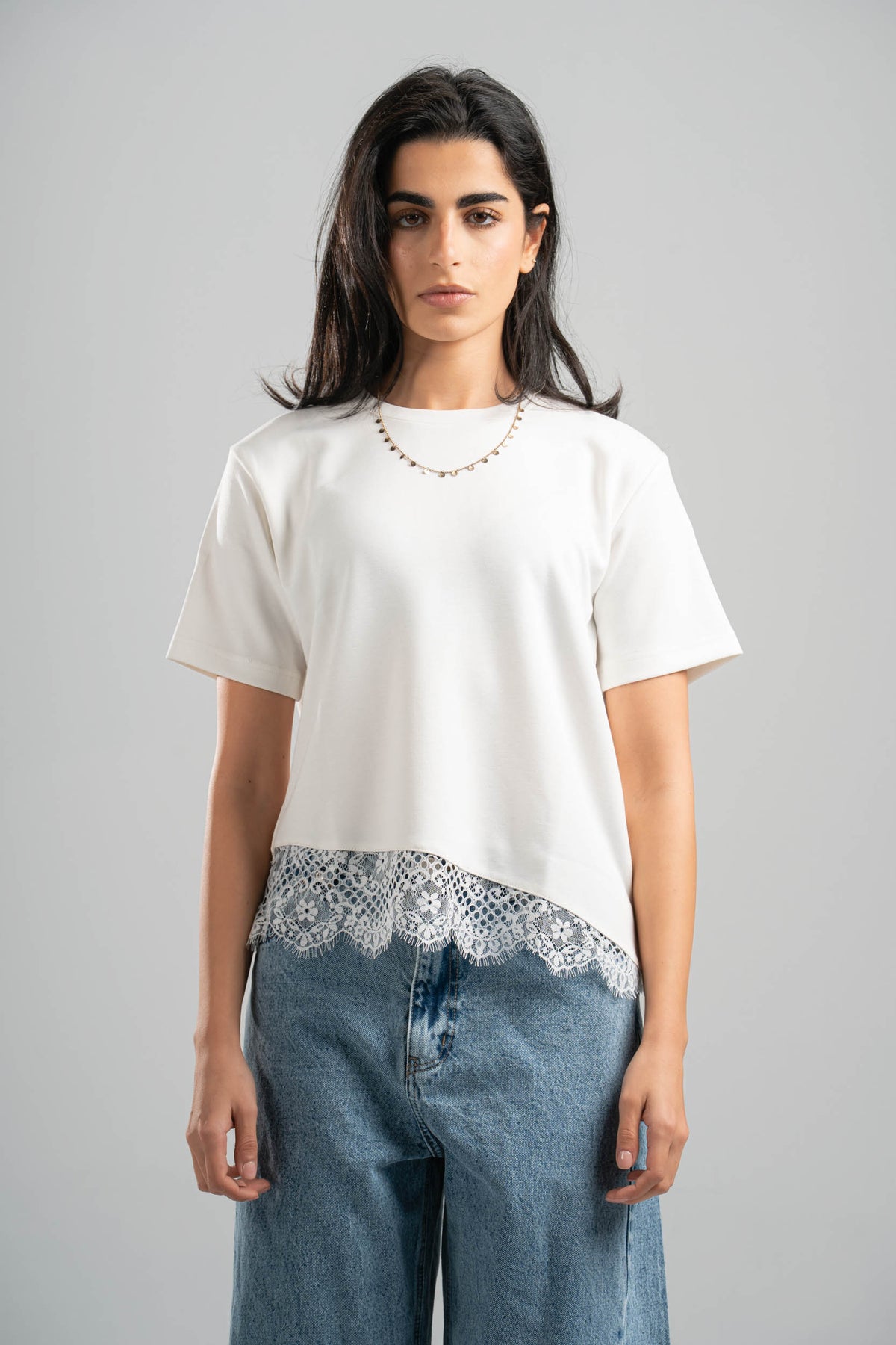 Woman wearing a white t-shirt with lace trim and blue jeans on a gray background