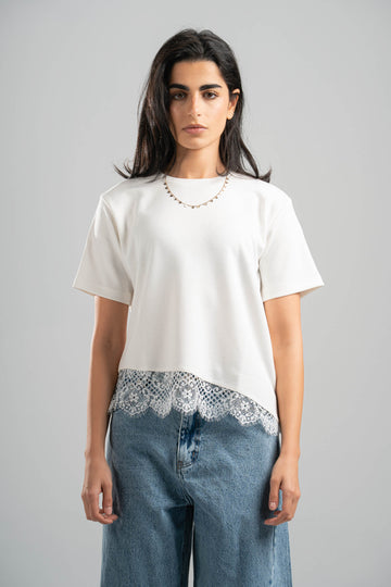 Woman wearing a white t-shirt with lace trim and blue jeans on a gray background
