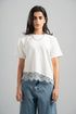 Woman wearing a white t-shirt with lace trim and blue jeans on a gray background