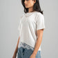 Woman wearing a white t-shirt with lace trim and blue jeans on a gray background