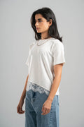 Woman wearing a white t-shirt with lace trim and blue jeans on a gray background