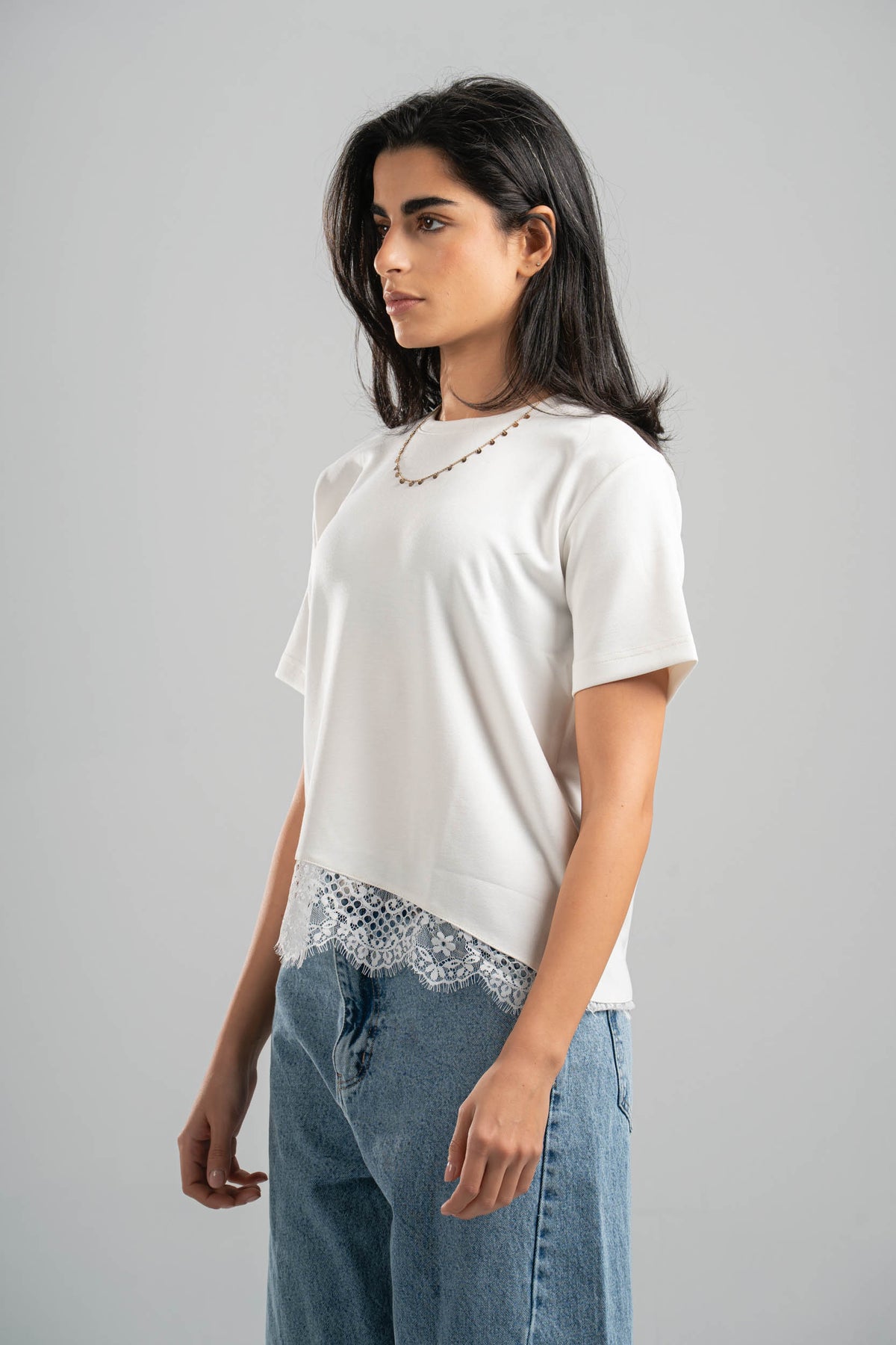 Woman wearing a white t-shirt with lace trim and blue jeans on a gray background