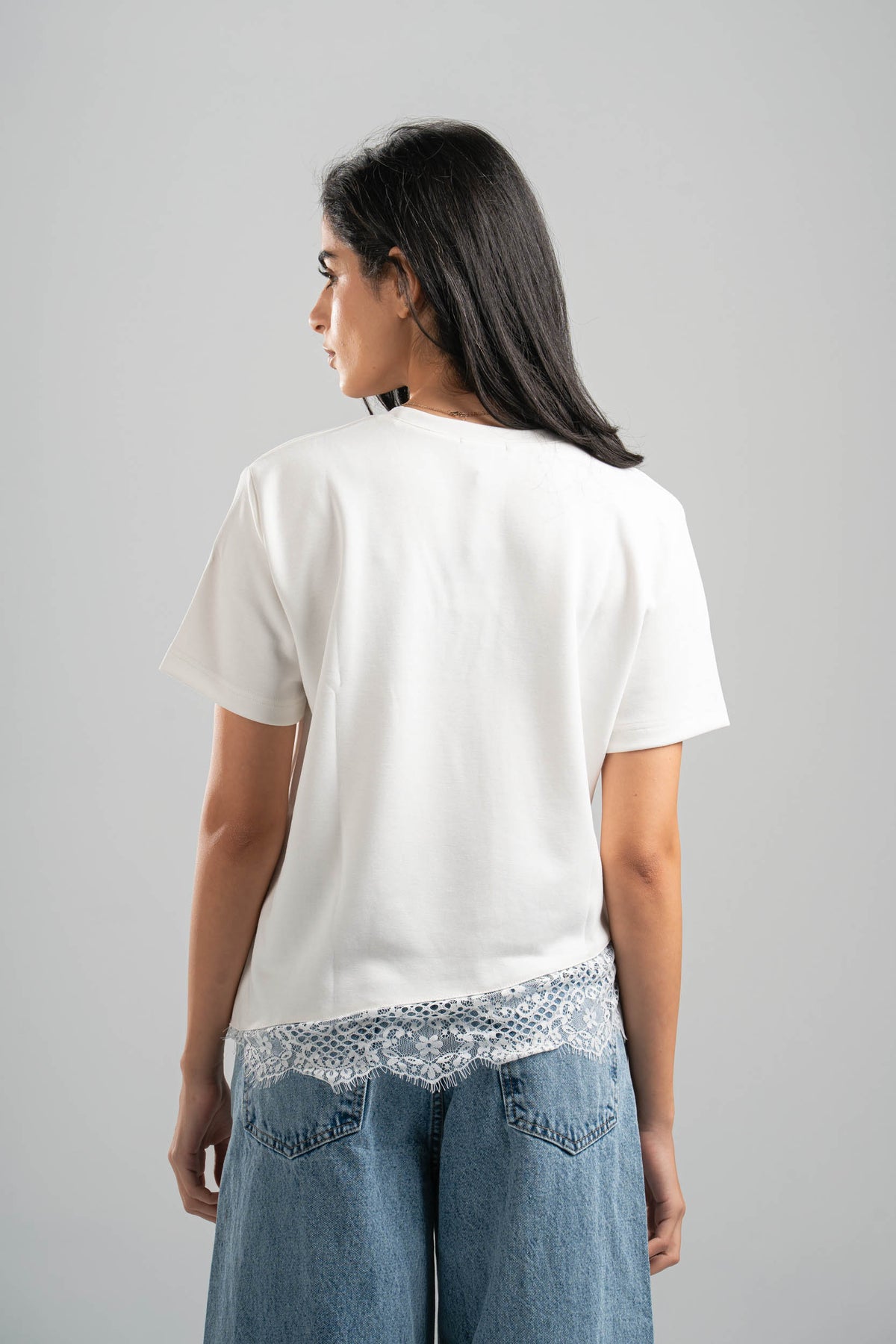 Person wearing a white t-shirt and blue jeans with lace trim on a gray background