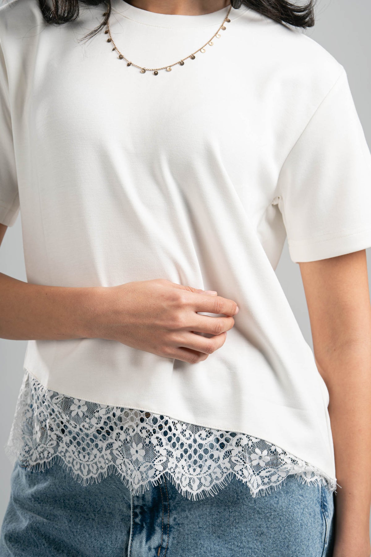 White t-shirt with lace trim worn by a person on a gray background