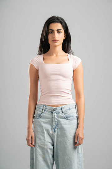 Woman wearing a light pink top and light blue jeans against a gray background