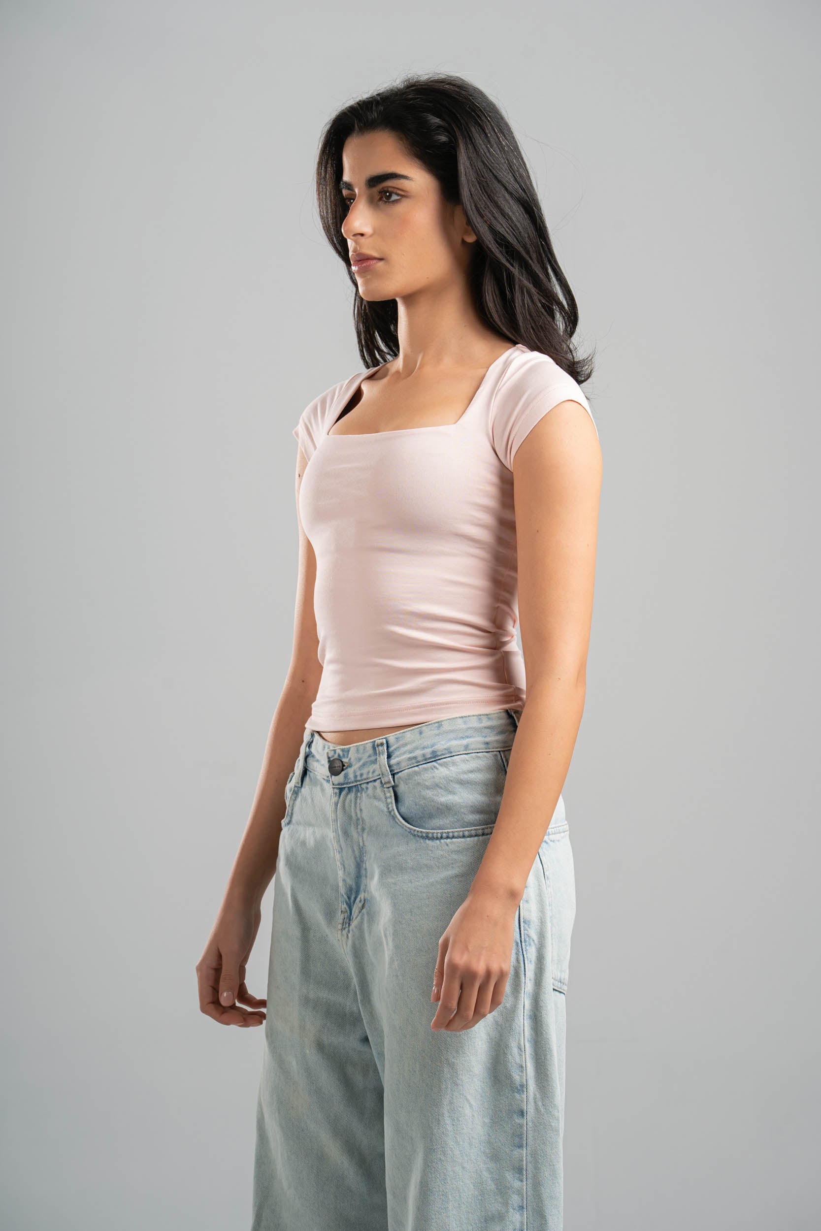 Woman wearing a light pink top and light blue jeans on a gray background