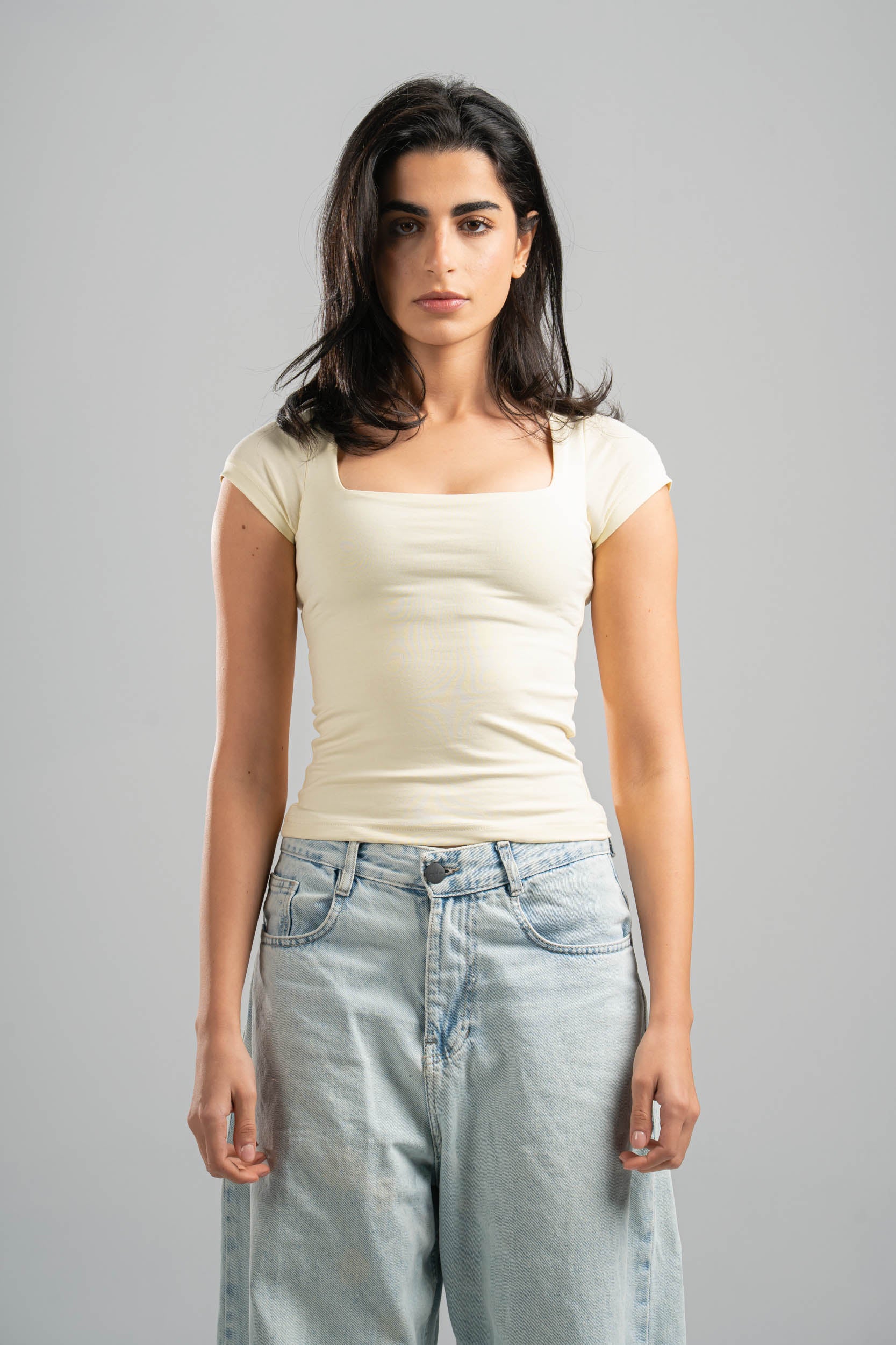 Woman wearing a white top and light blue jeans against a gray background