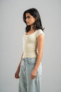 Woman wearing a beige top and light blue jeans against a gray background