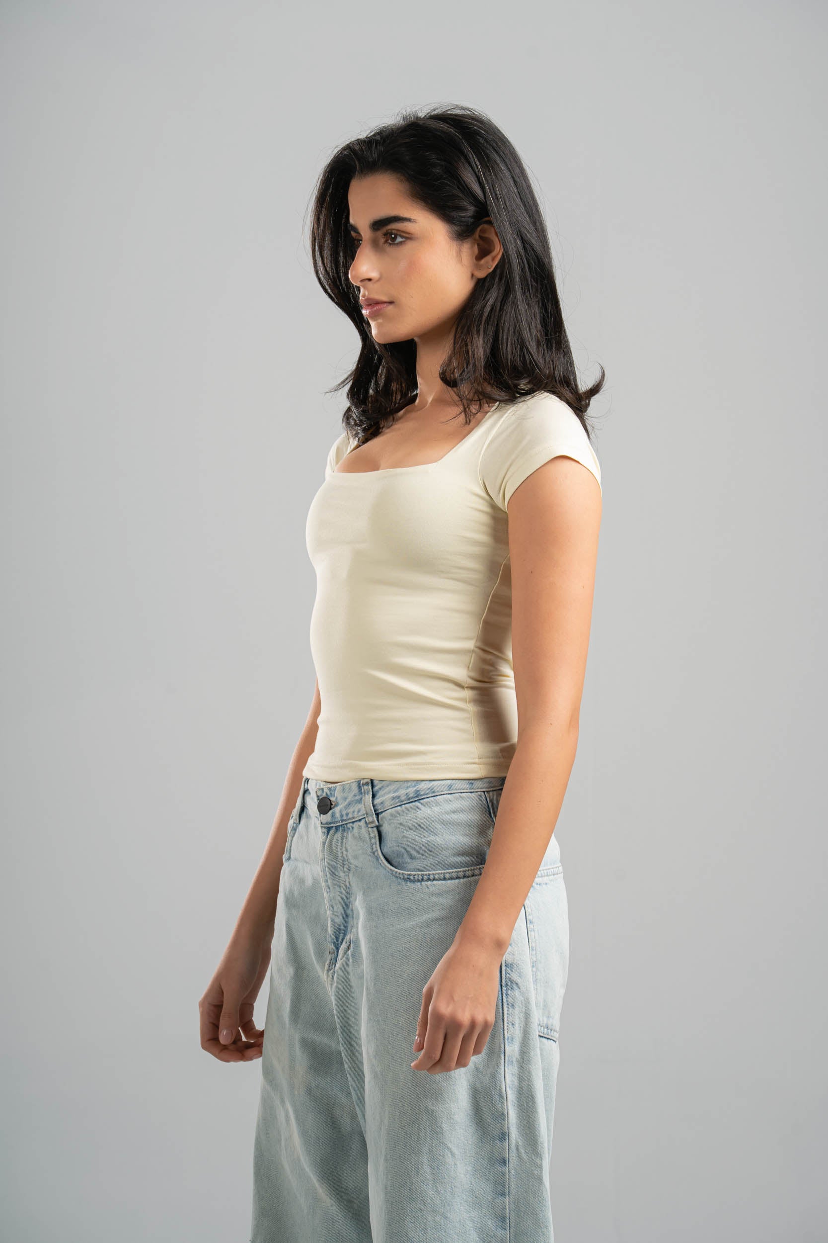 Woman wearing a beige top and light blue jeans against a gray background