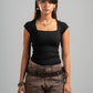 Woman wearing a black top and brown pants against a gray background