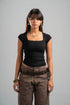 Woman wearing a black top and brown pants against a gray background