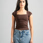 Woman wearing a brown top and blue jeans against a gray background