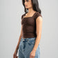 Woman wearing a brown top and blue jeans against a gray background