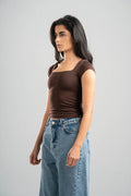 Woman wearing a brown top and blue jeans against a gray background