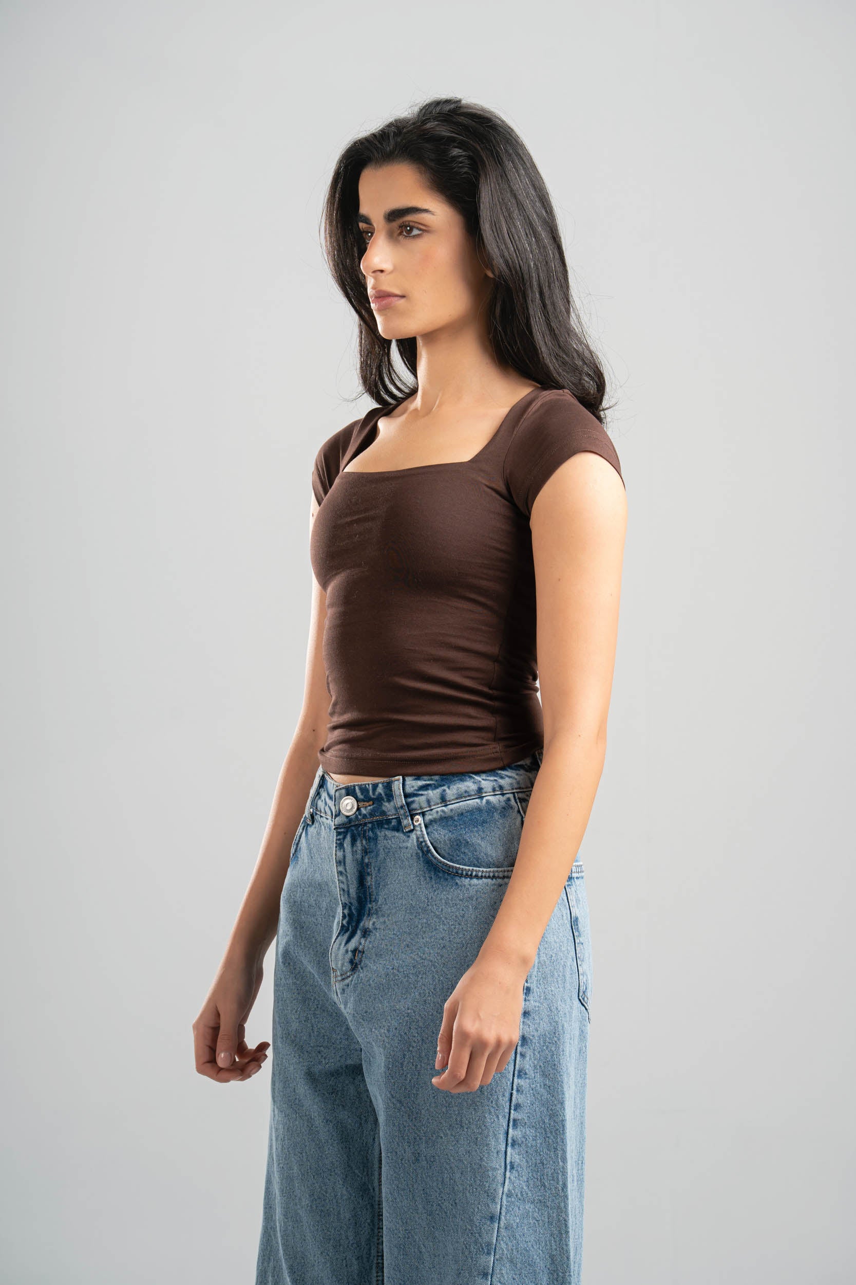 Woman wearing a brown top and blue jeans against a gray background