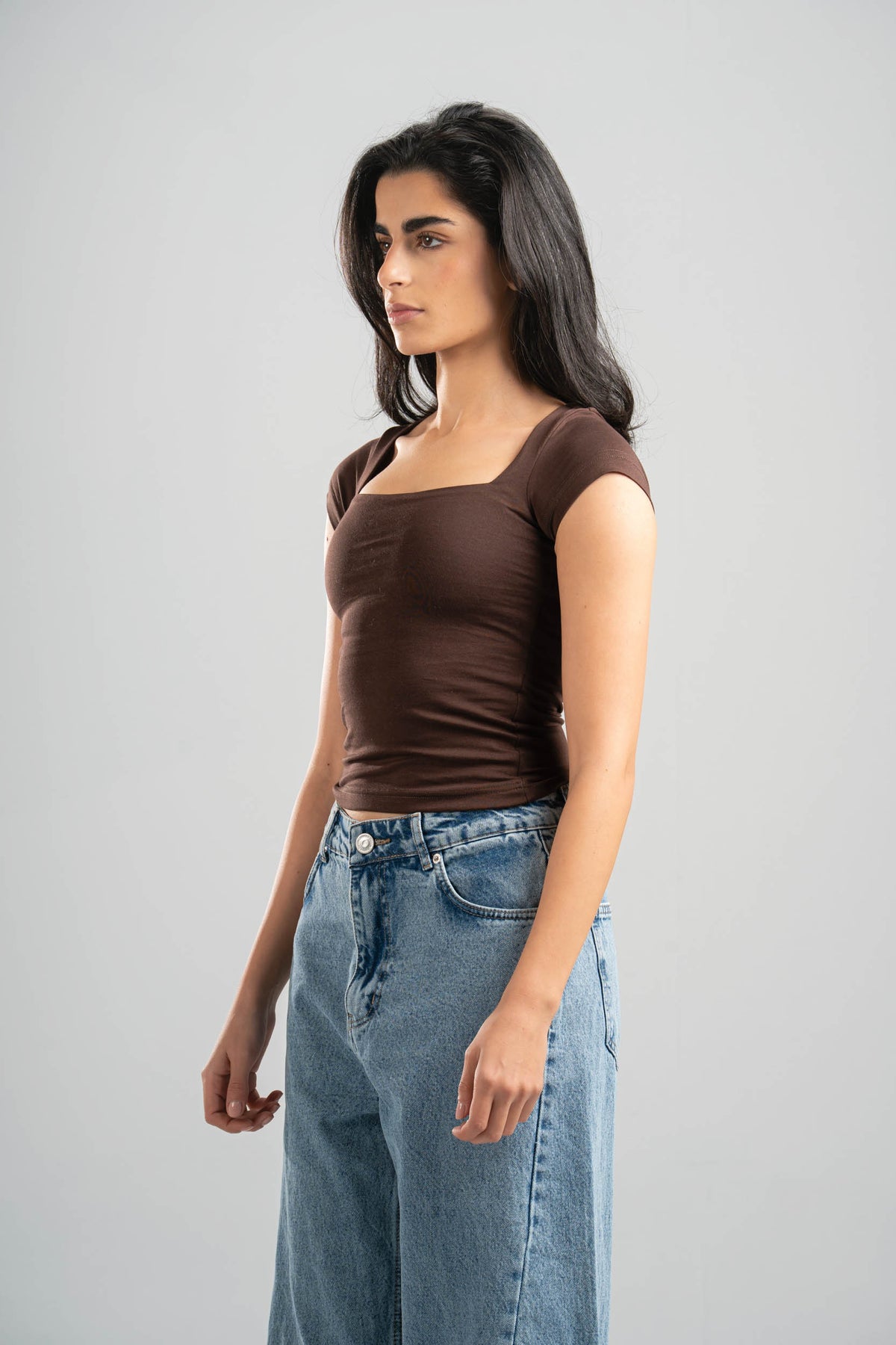 Woman wearing a brown top and blue jeans against a gray background