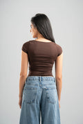 Woman wearing a brown top and blue jeans against a gray background