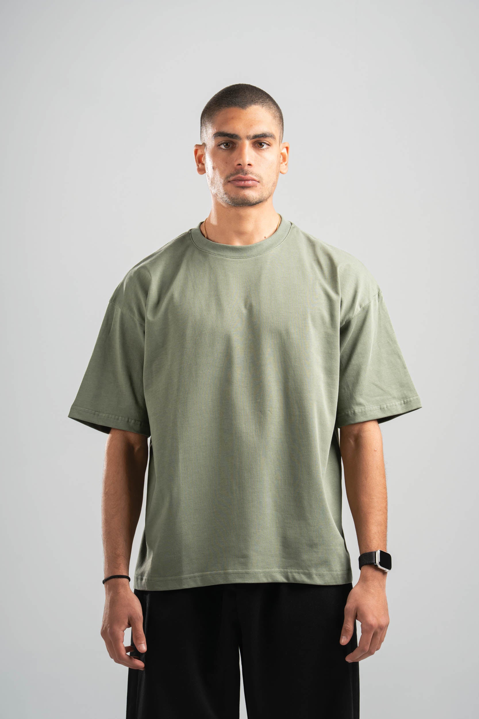 Man wearing a green t-shirt and black pants against a gray background