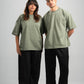 Two people wearing matching green t-shirts and black pants on a plain background