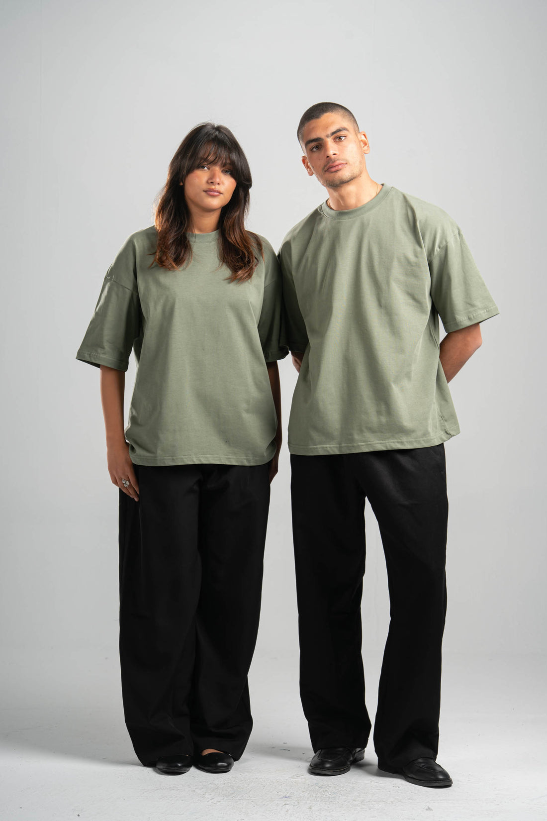 Two people wearing matching green t-shirts and black pants on a plain background
