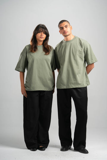 Two people wearing matching green t-shirts and black pants on a plain background