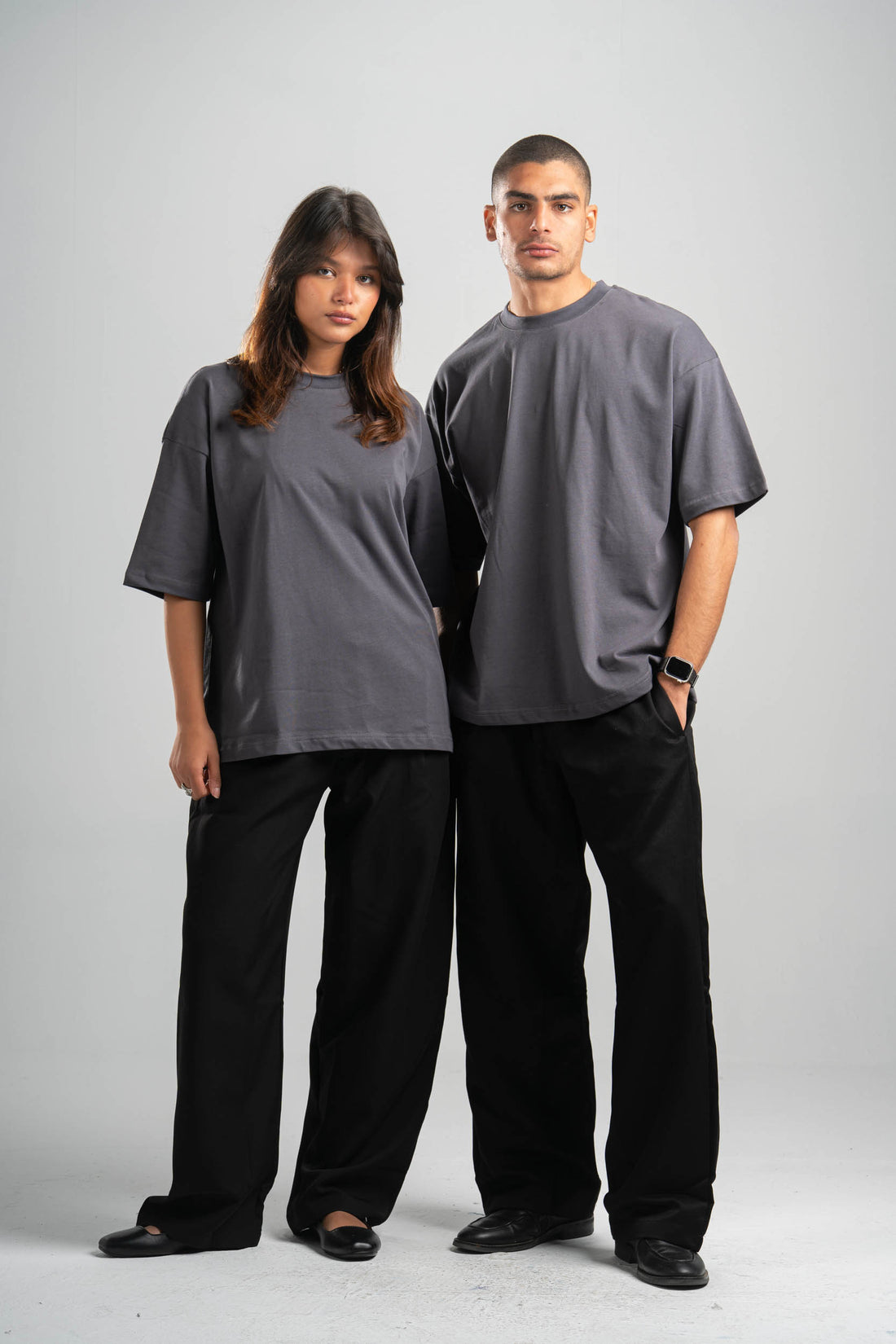 Two people wearing matching gray t-shirts and black pants on a white background