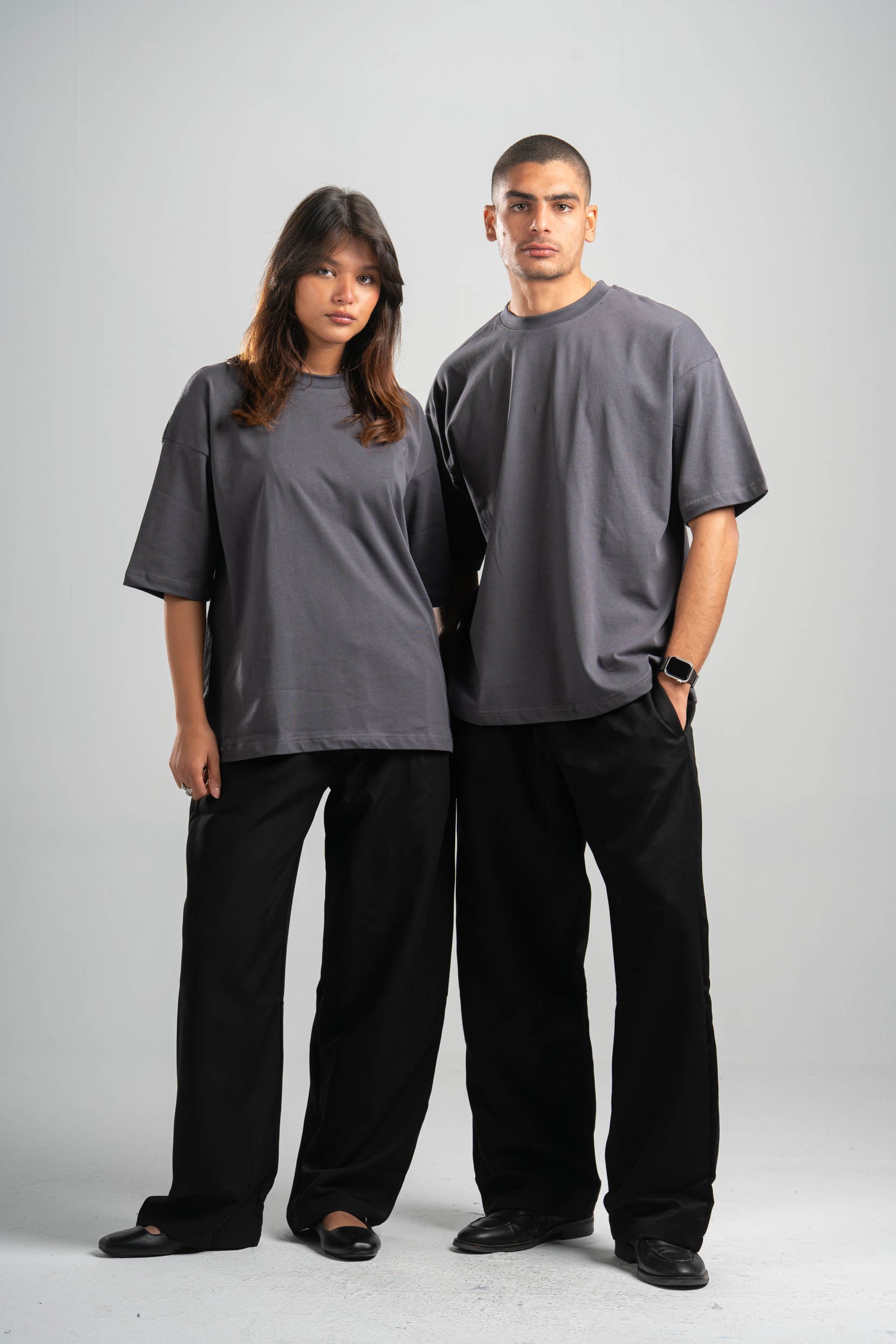 Two people wearing matching gray t-shirts and black pants on a white background