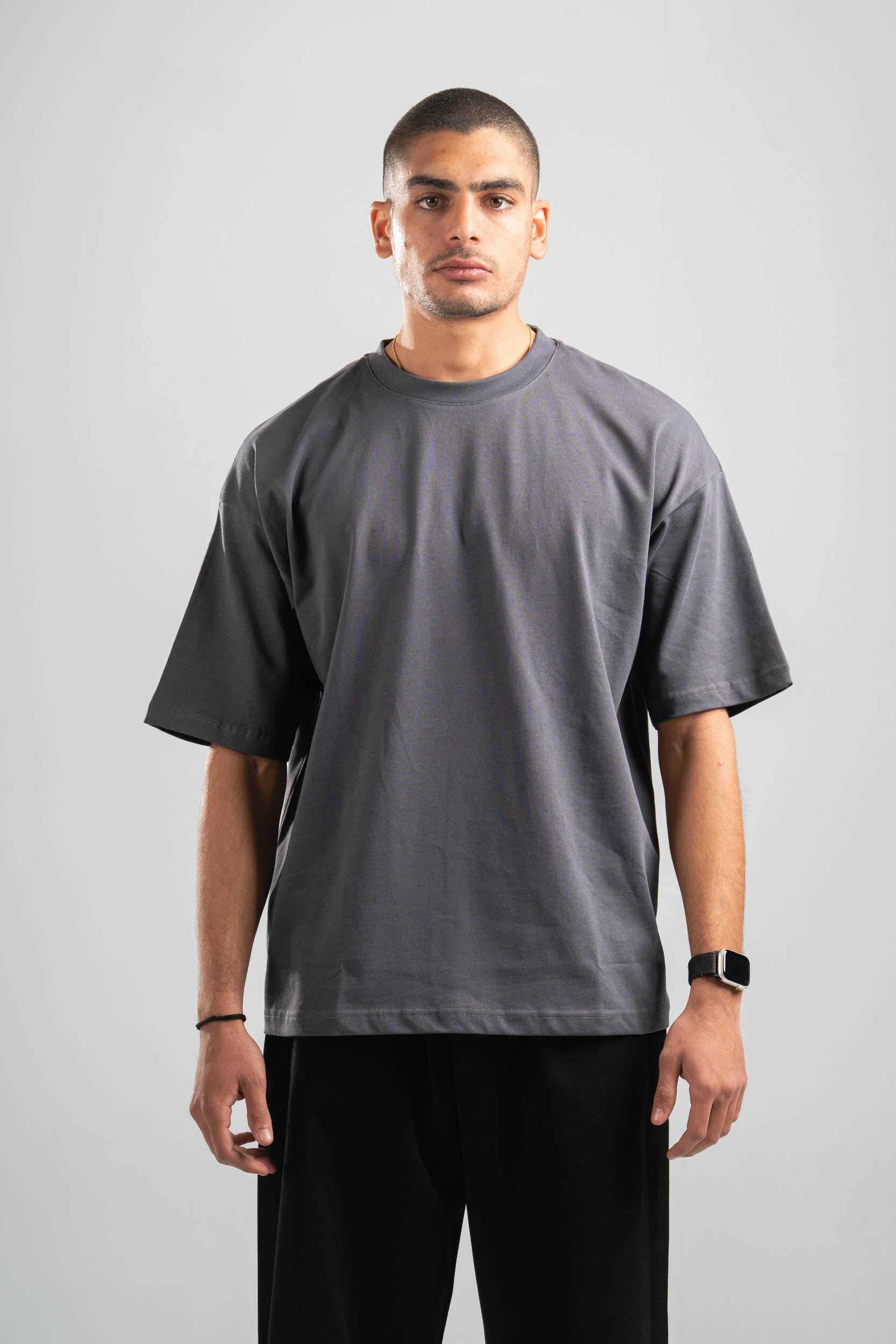 Man wearing a plain gray t-shirt and black pants on a light gray background