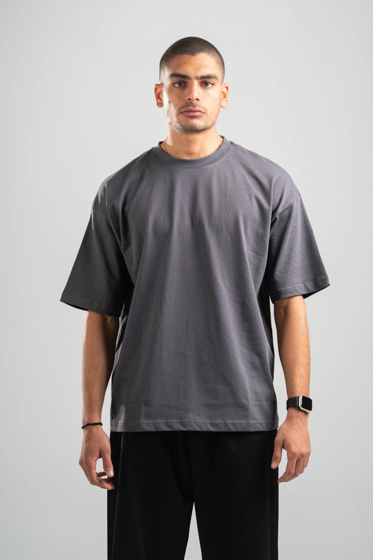 Man wearing a plain gray t-shirt and black pants on a light gray background