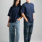 Two people wearing navy t-shirts and jeans standing against a gray background