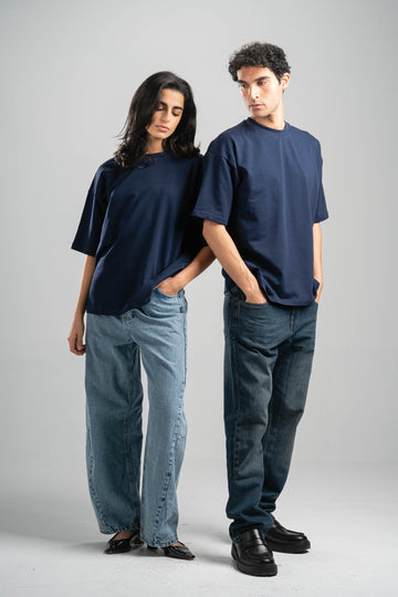 Two people wearing navy t-shirts and jeans standing against a gray background