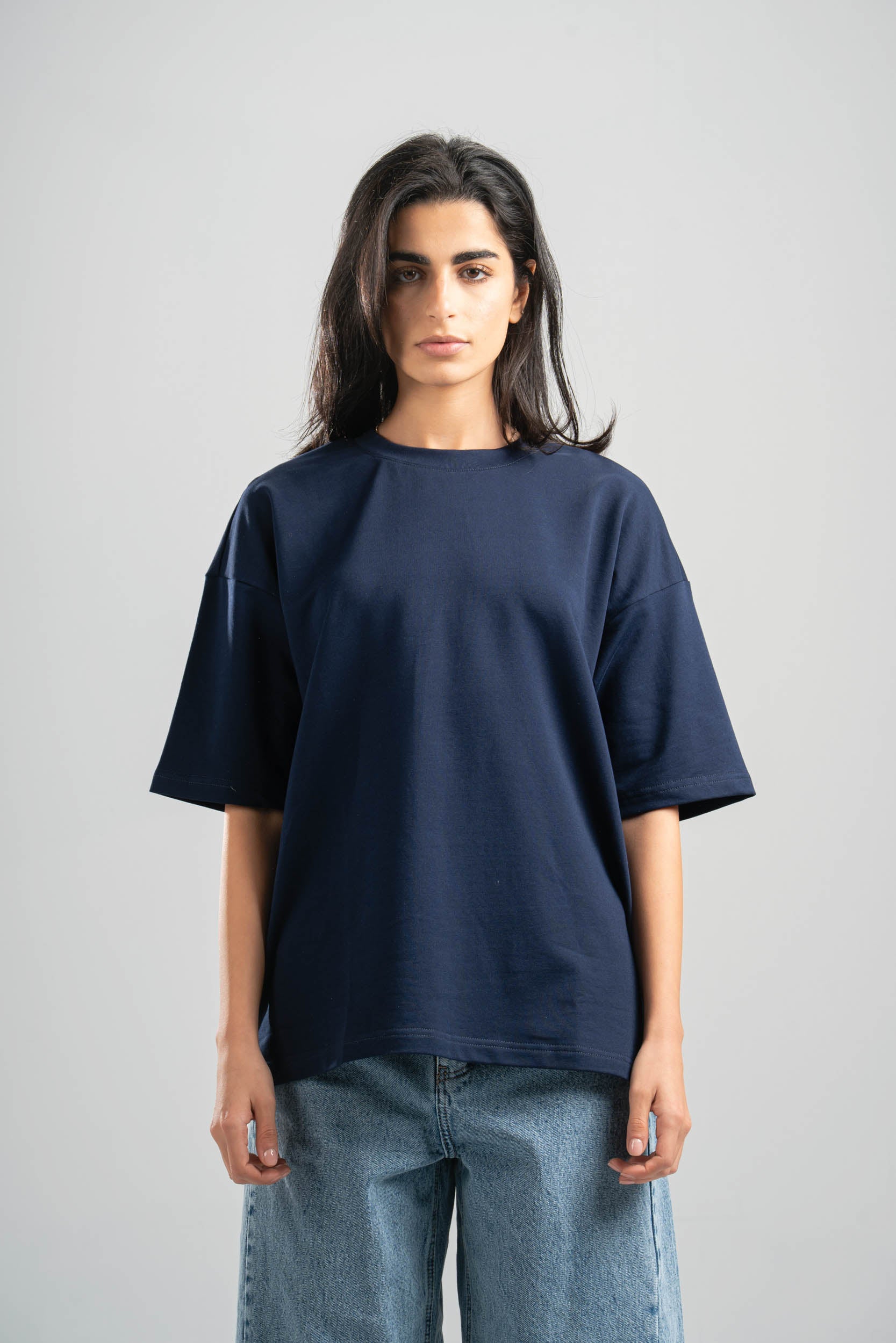 Person wearing a navy blue t-shirt and jeans on a gray background