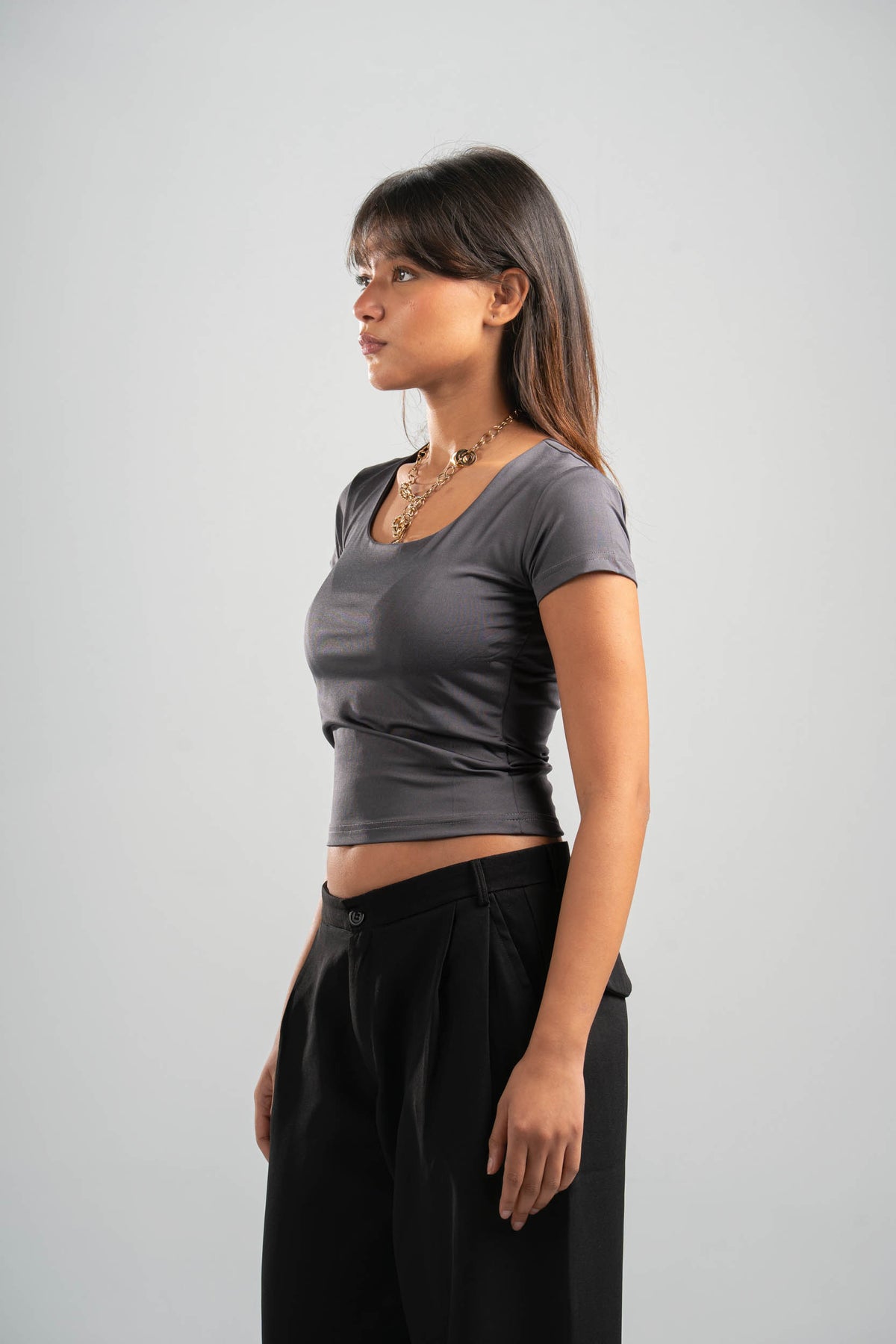 Woman wearing a gray crop top and black pants on a light gray background