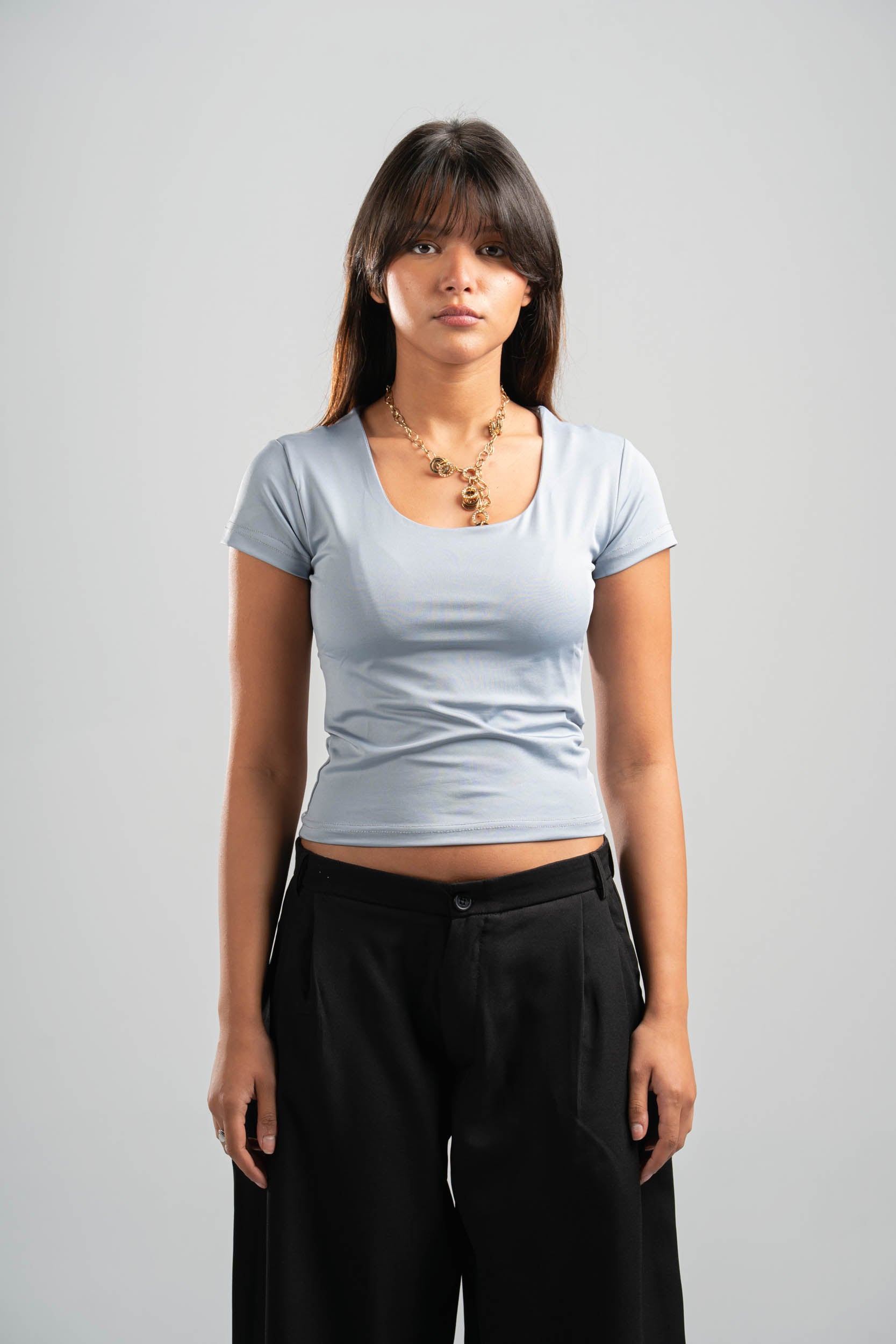 Woman wearing a light blue t-shirt and black pants on a gray background