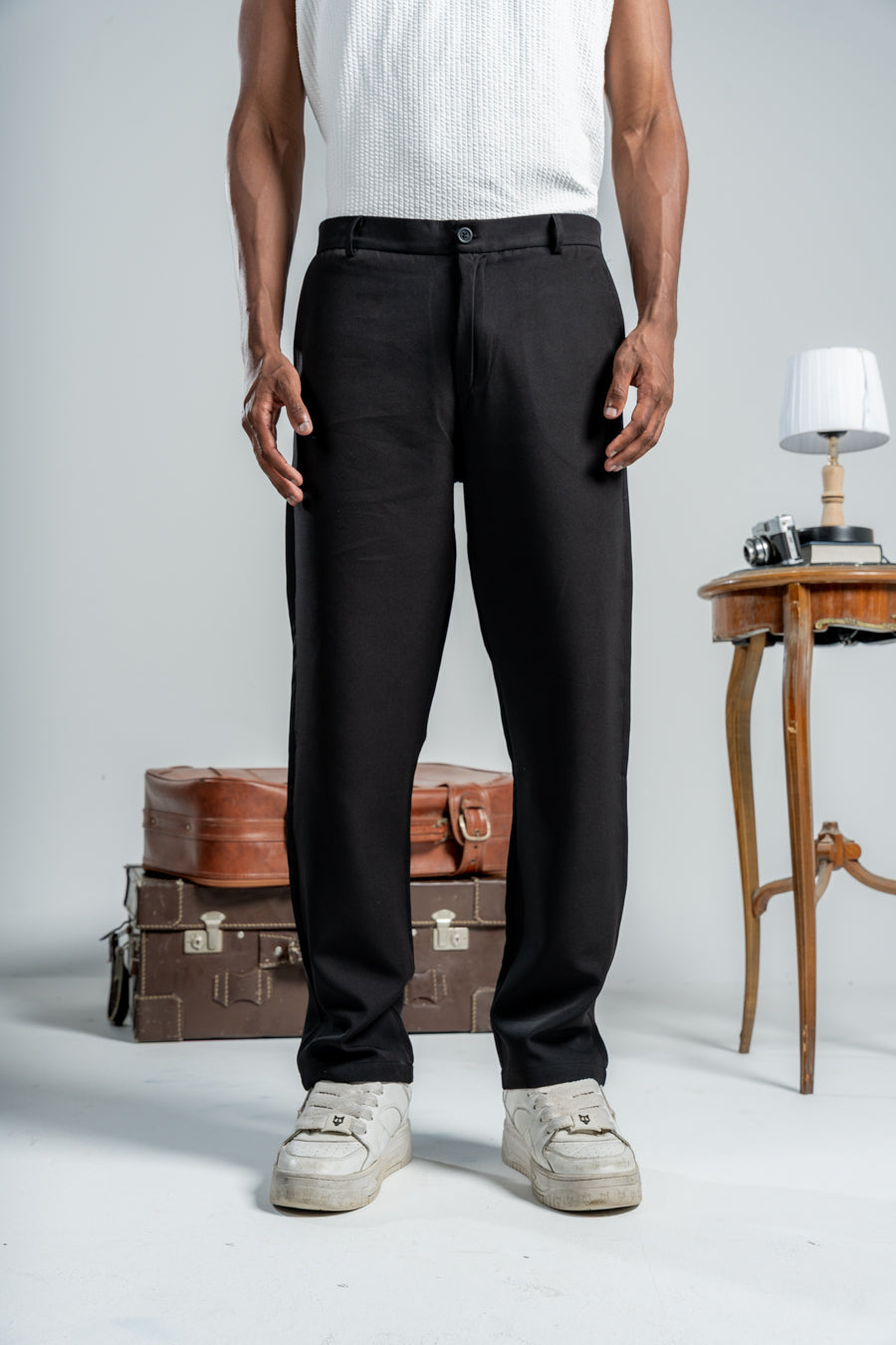 Person wearing black pants standing in a minimalistic setting with vintage suitcases and a table.