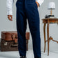 Person wearing a white shirt and navy pants standing in front of vintage suitcases and a small table.