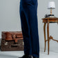 Person wearing navy pants with a white shirt, standing next to vintage suitcases and a small table.