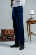 Person wearing navy pants with a white shirt, standing next to vintage suitcases and a small table.