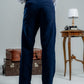 Person wearing navy pants and a white shirt with a gray background, standing next to vintage suitcases and a small table.